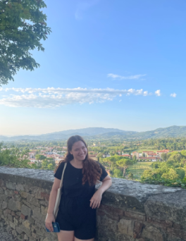 Woman in a black dress in front of a village and blue sky.