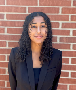 Woman wearing a blazer in front of a red brick wall.