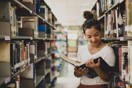 Woman reading among book shelves.