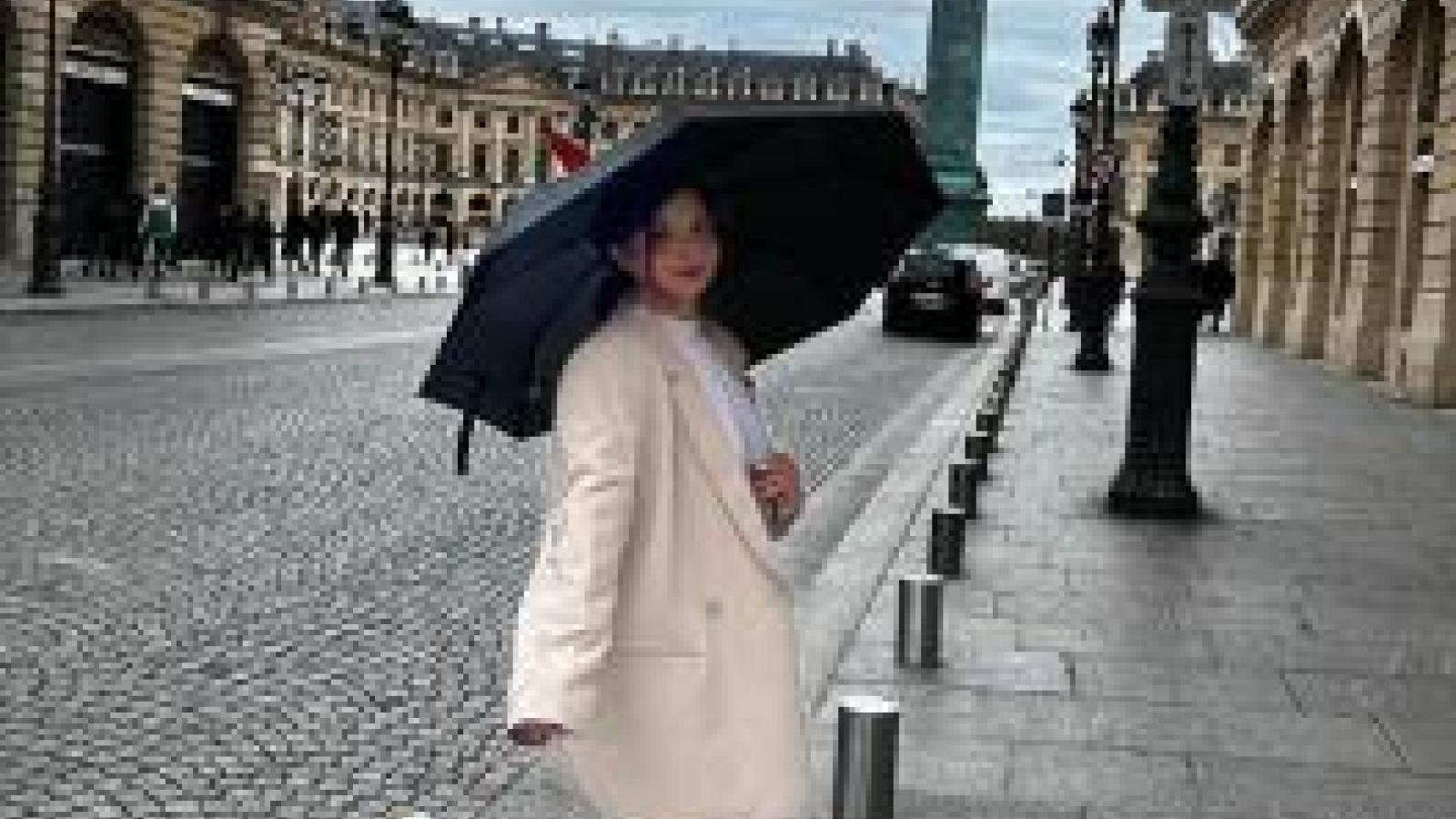 Woman in a cream coat with black umbrella on a street.